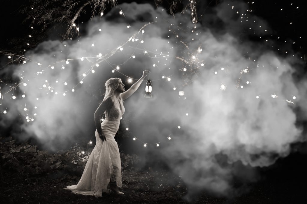Creative black and white bridal portrait holding lantern under a willow tree at night with white smoke