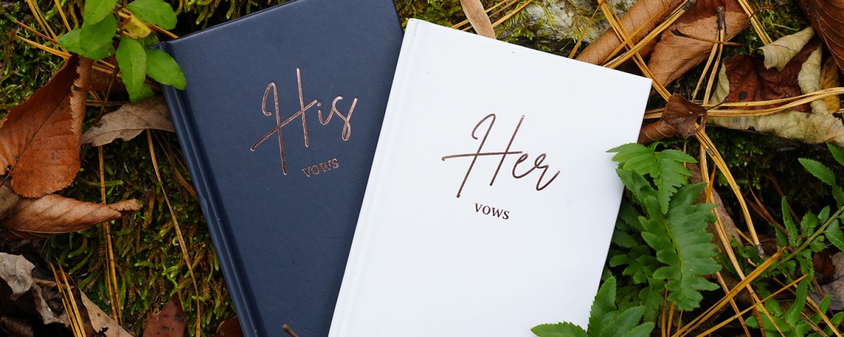 His and Her vow books laying on a forest floor with ferns