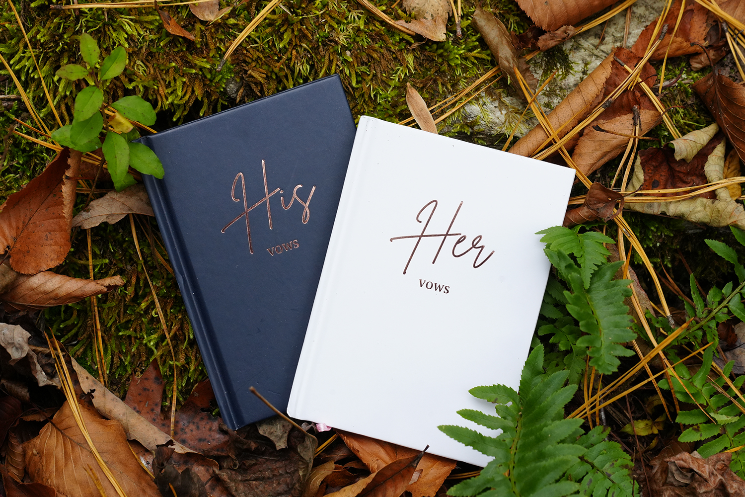 His and Her vow books laying on a forest floor with ferns
