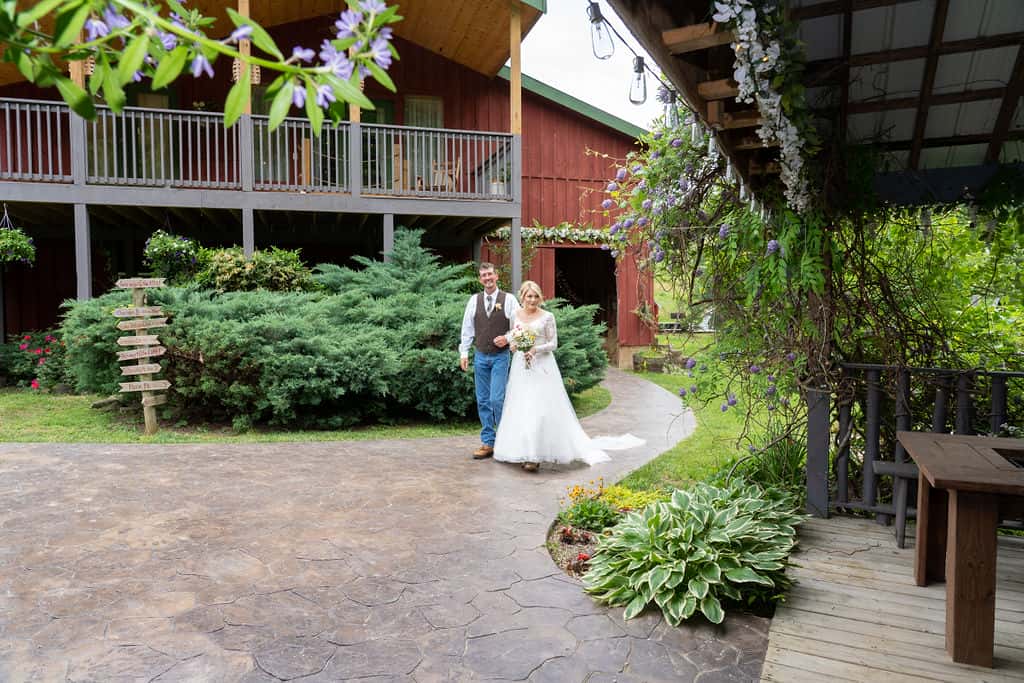 Bride walking from barn wedding venue along a stone sidewalk to a covered pavilion ceremony area