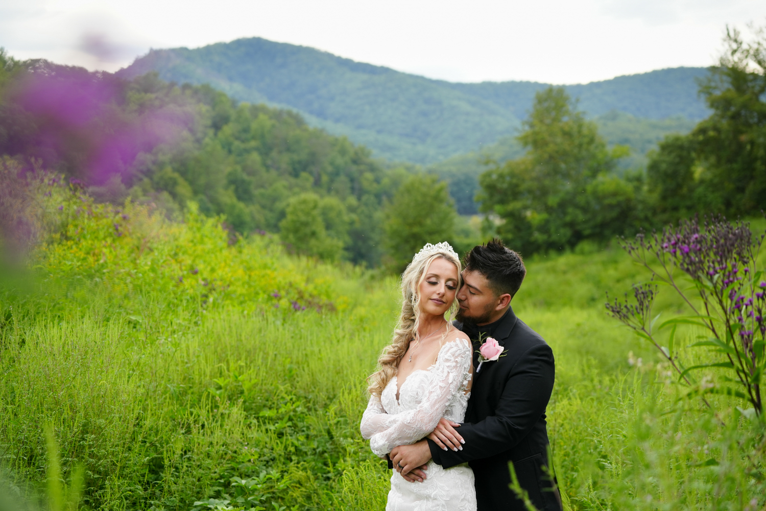 Groom holding his bride passionately in a meadow with a mountain view