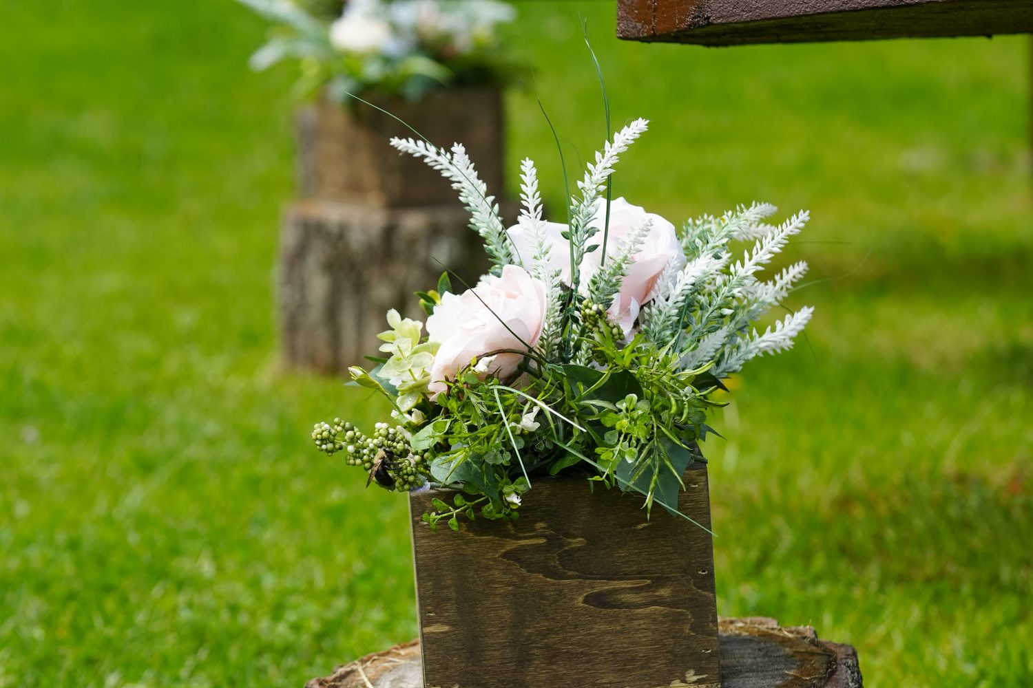 Silk greenery with white and pink flowers in wooden boxes sitting on top of stumps at a wedding venue called Honeysuckle Hills in Pigeon Forge