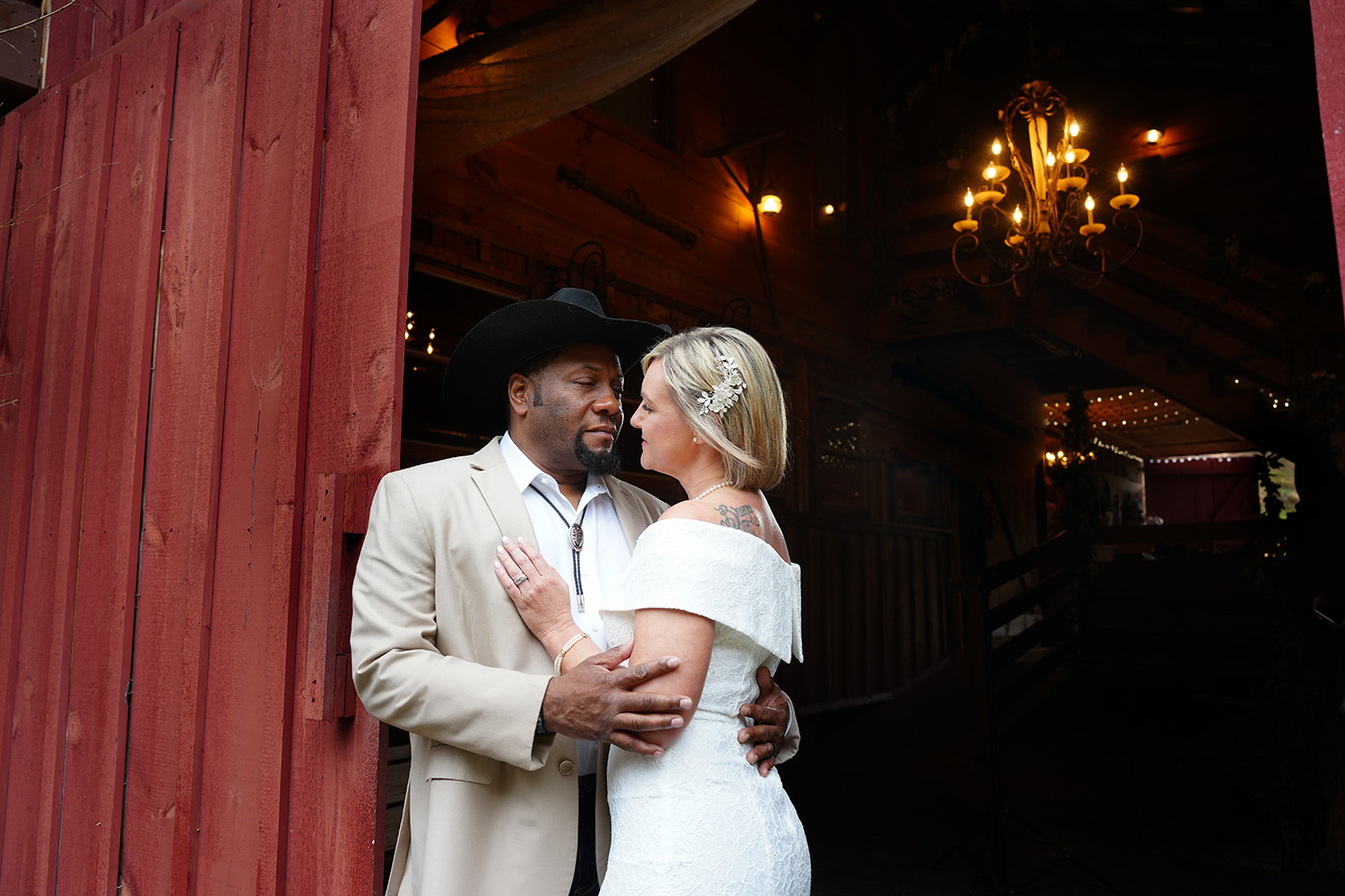 Sexy portrait of a wedding couple at a red barn door with a chandelier behind them