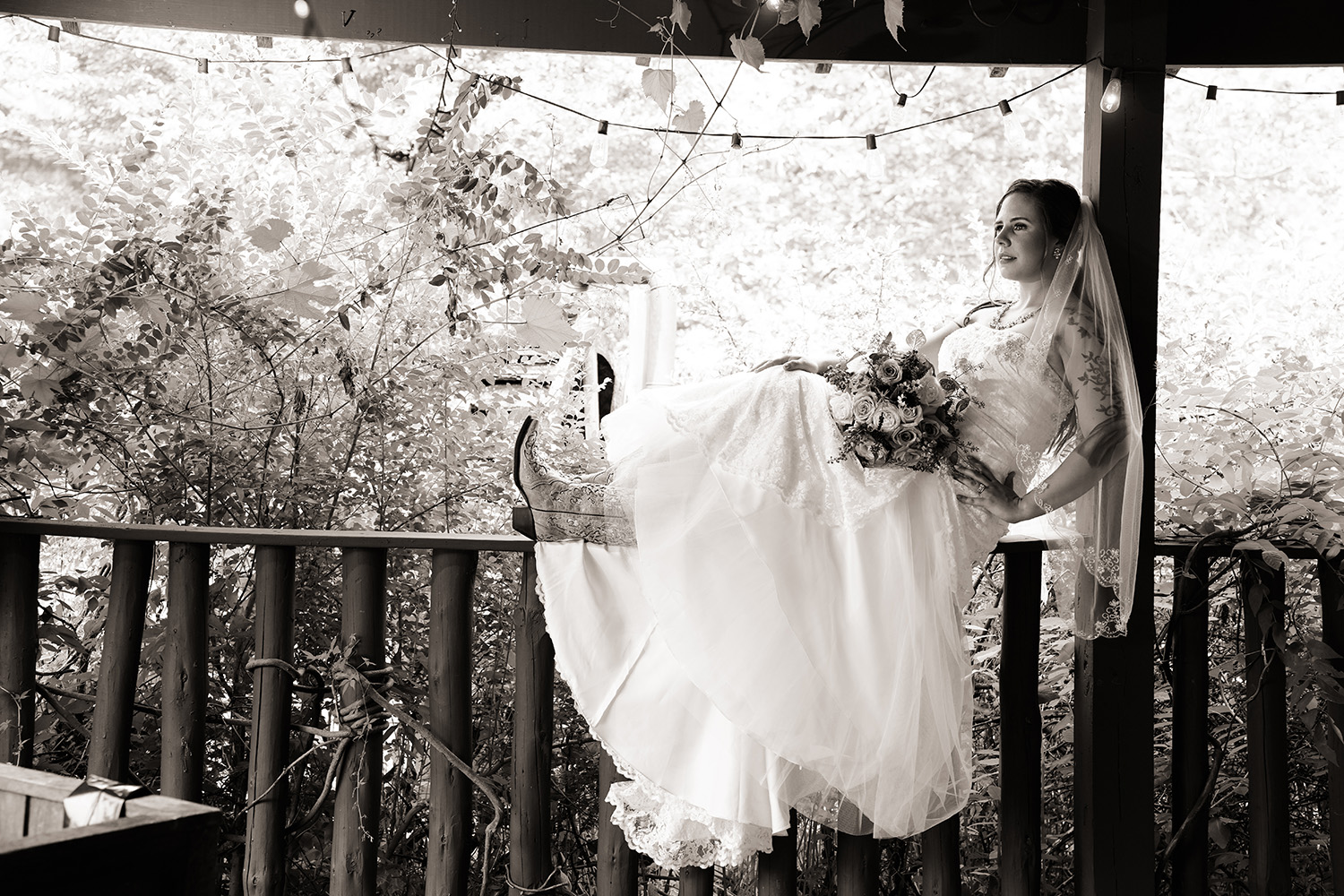 Black and white portrait of a bride sitting on a railing ledge