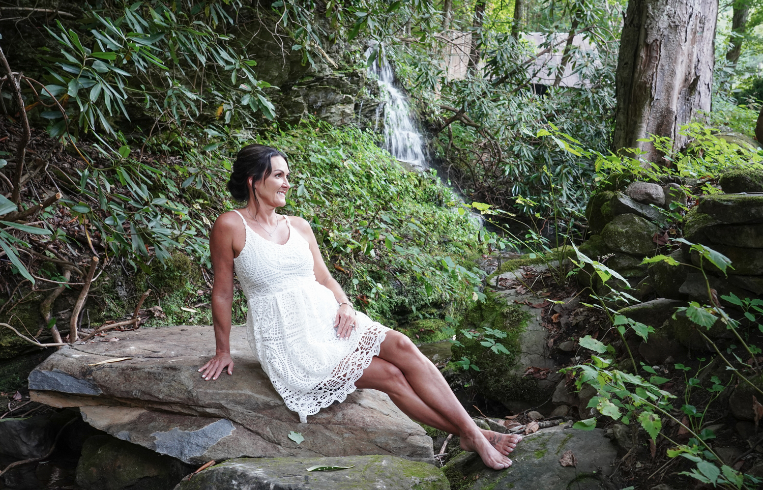 bride in short summer dress sitting on a rock in the Smoky Mountains by a waterfall