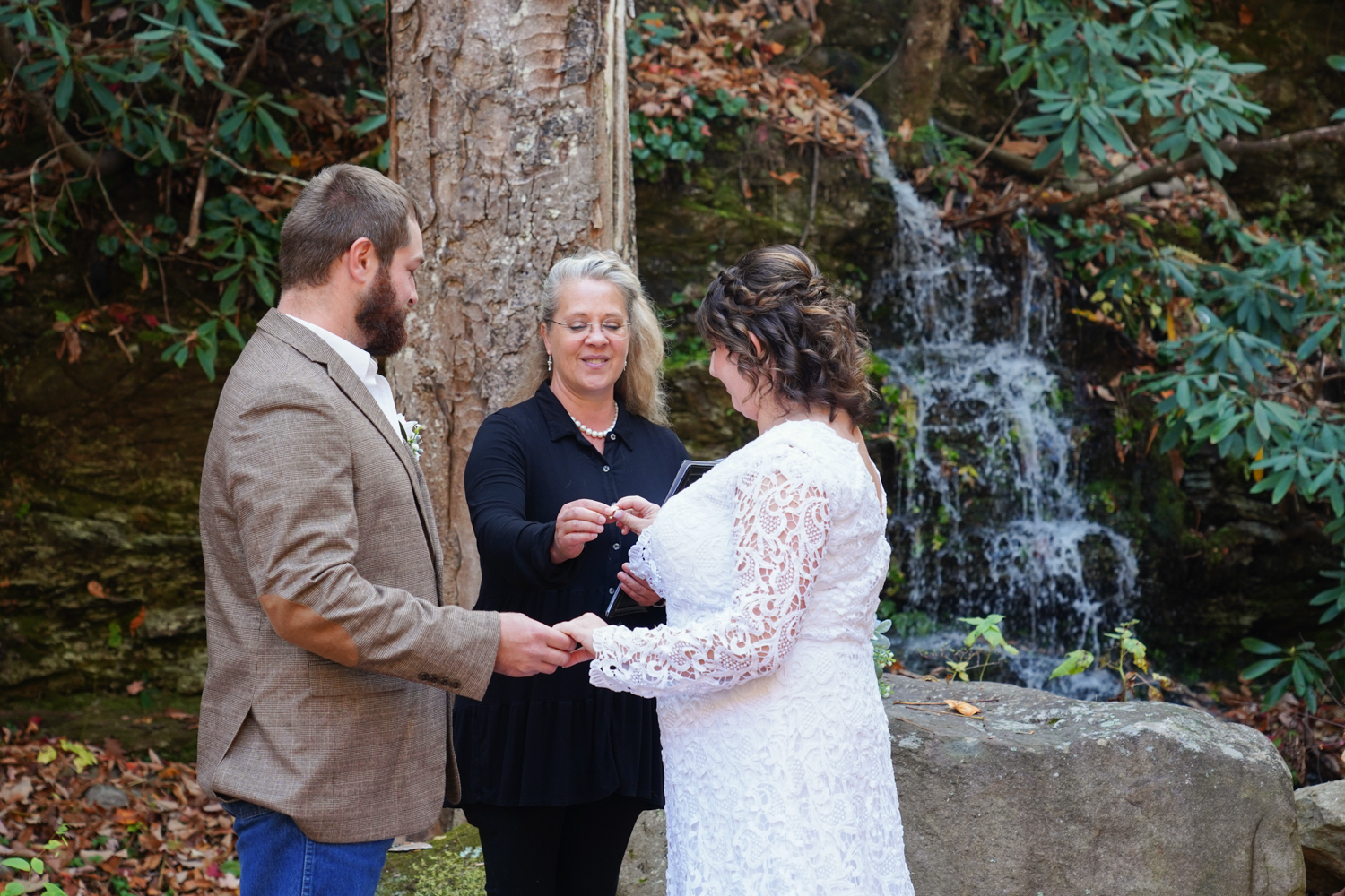Officiant Regina Starkey handing a ring to a bride at a Smoky Mountain waterfall ceremony site in Pigeon Forge