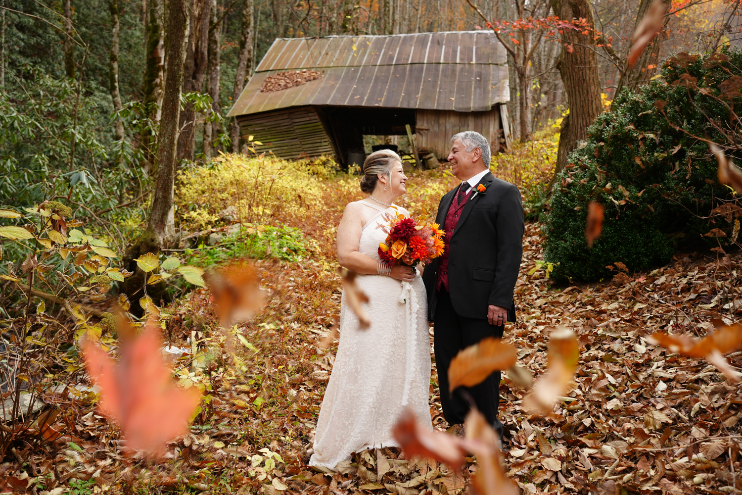 wedding couple walking with leaves falling in autumn and an old leaning barn behind them