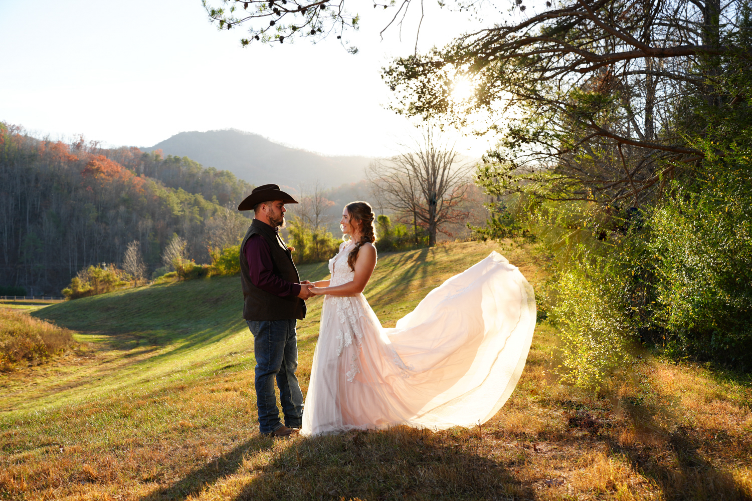 Bride's dress flowing in the wind in a field with a mountain view on her wedding day as she holds her groom's hand