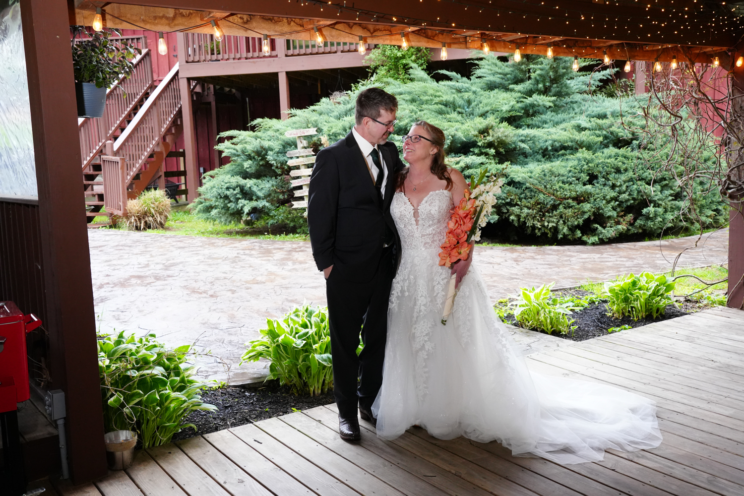 Wedding couple smiling at each other beneath a rustic pavilion with warm lights above them