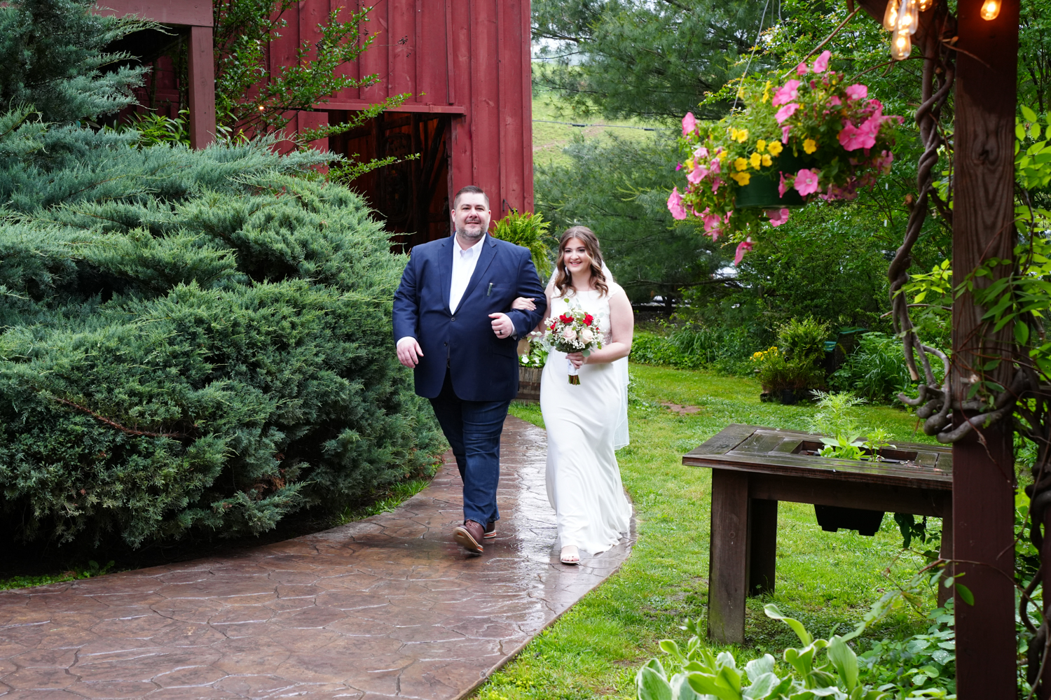 father walking his daughter along a sidewalk from a red barn in a garden