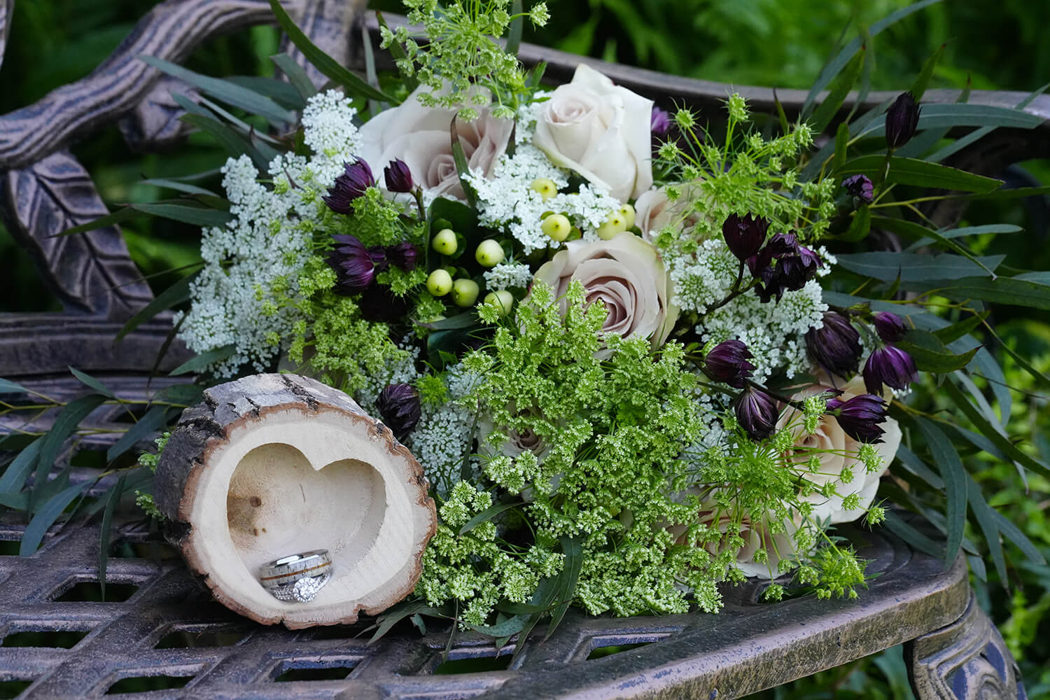 Wedding bouquet and rings sitting in a heart shaped wooden box on a metal bench at Honeysuckle Hills wedding venue