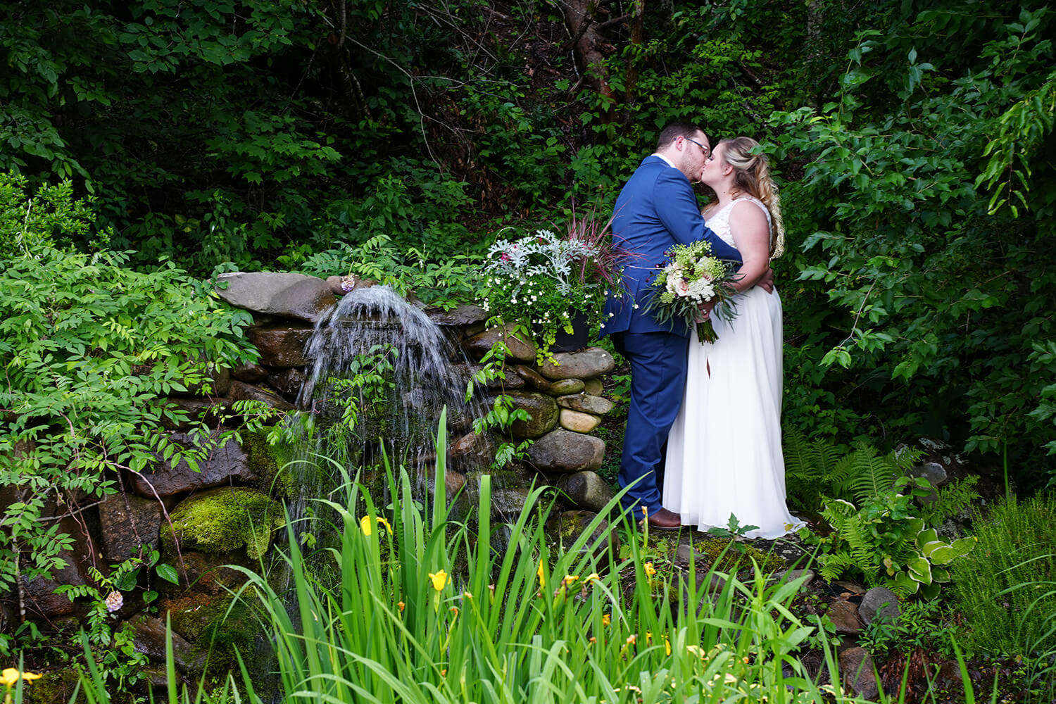 Wedding couple kissing at a pond with a waterfall and tall yellow water iris
