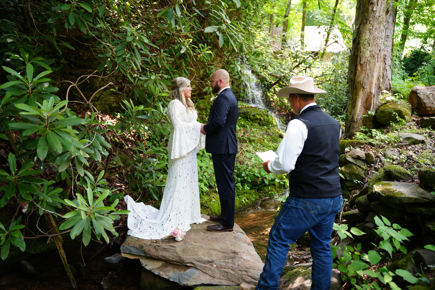 Pastor in cowboy hat marrying a couple standing on a rock by a waterfall in the mountains of Pigeon Forge