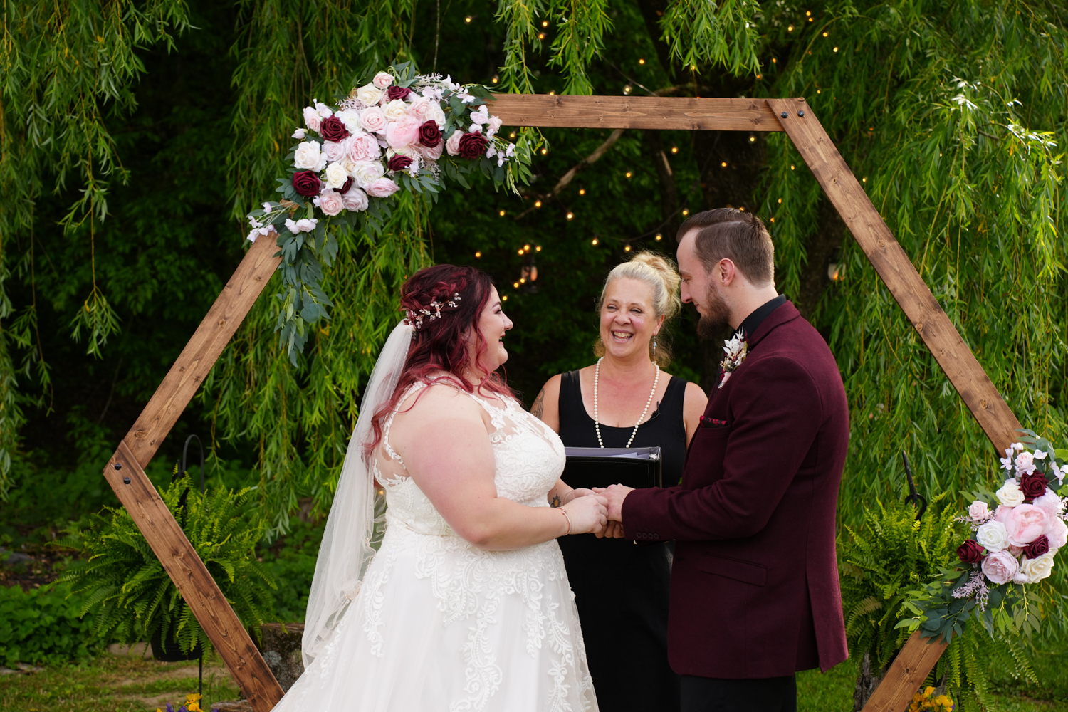 Woman ceremony officiant presiding over a wedding under a willow tree with a hexagon arbor