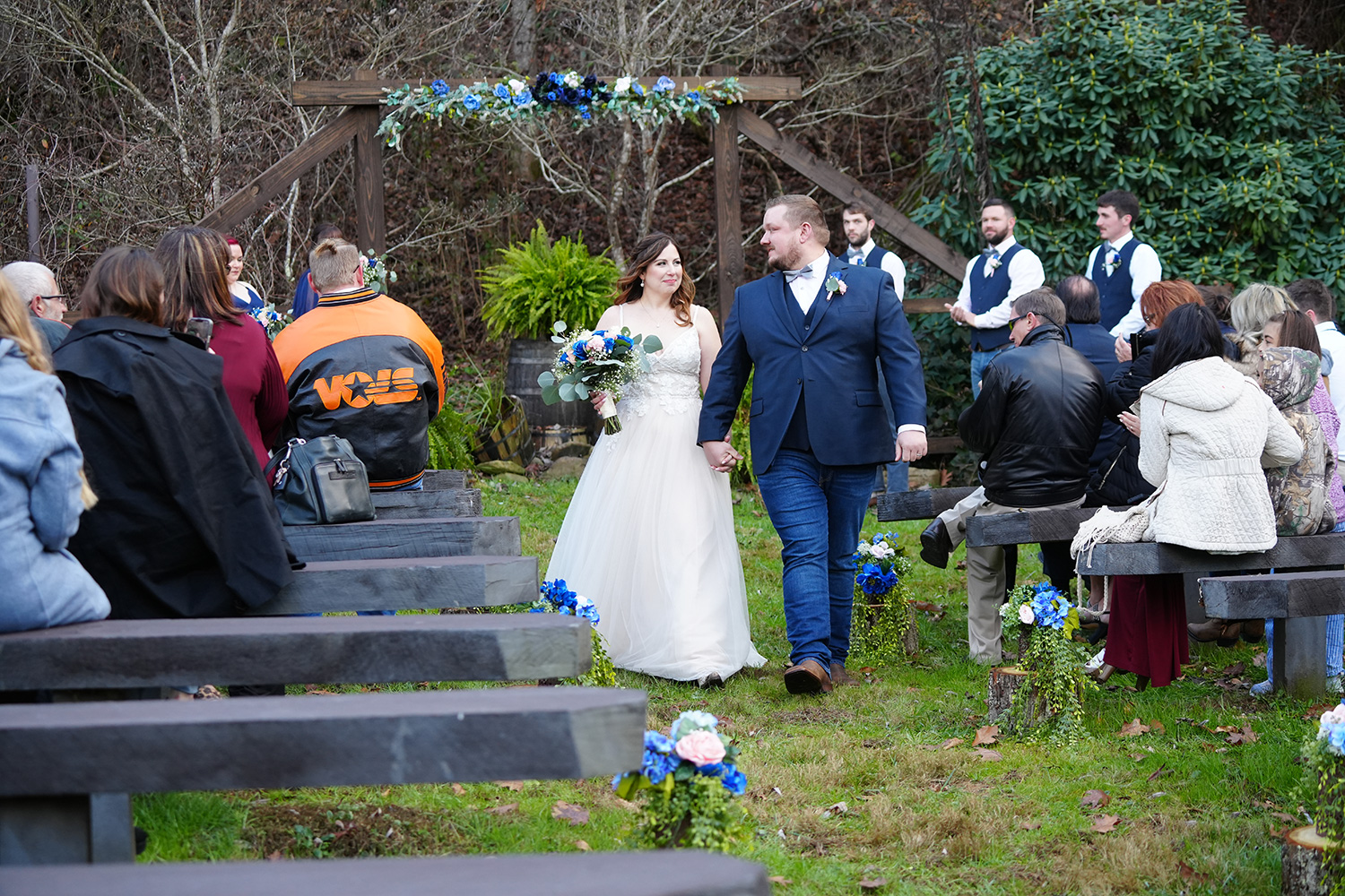 wedding couple walking back down the aisle in a forest by a wooden wedding arbor with blue flowers