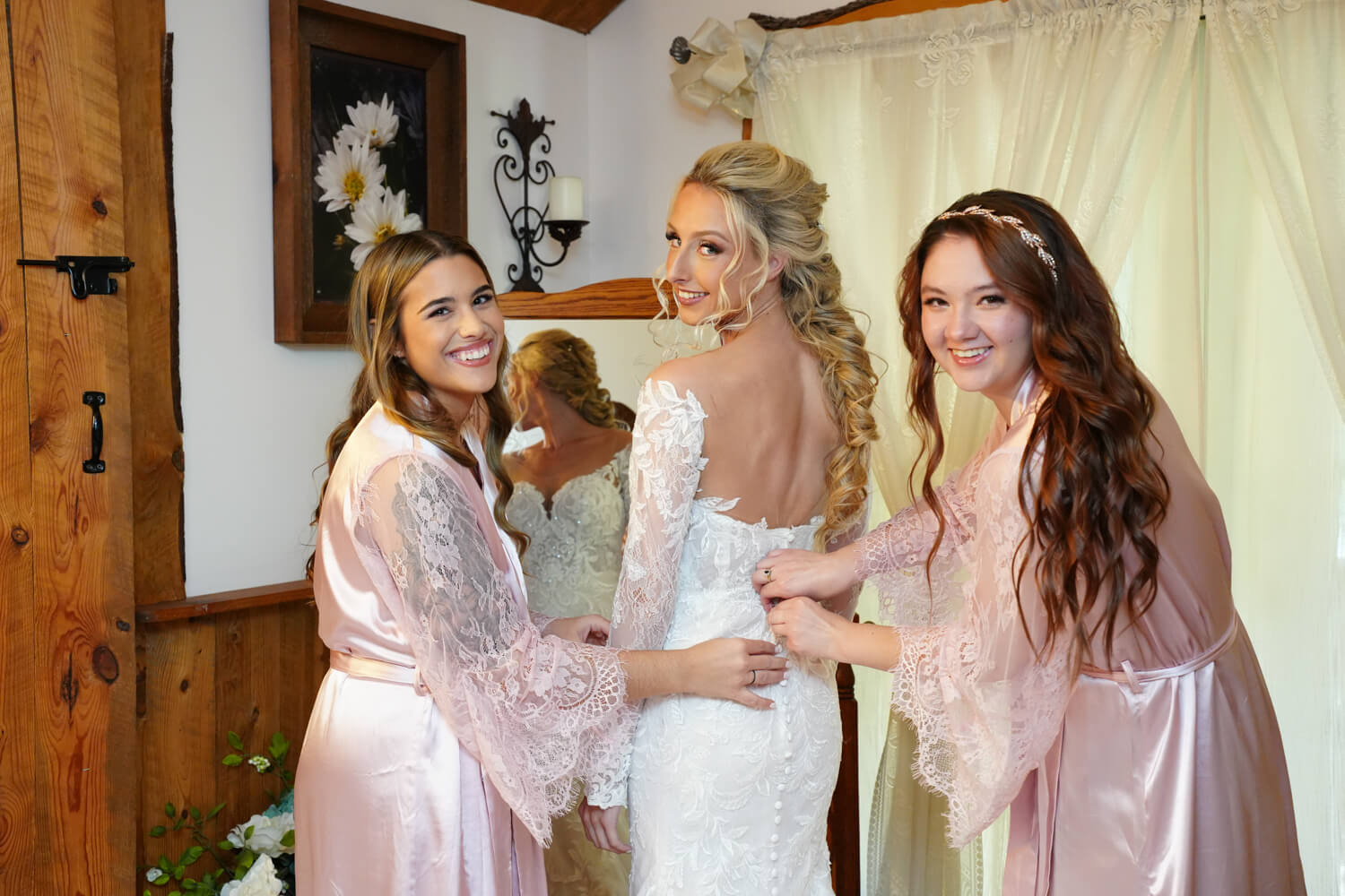Bridesmaids zipping up a bride's dress in front of a full length mirror