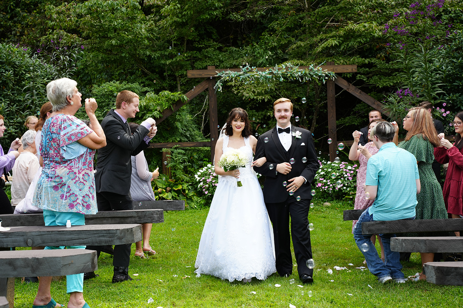wedding recessional with bubbles in the summer at a wooden wedding arbor