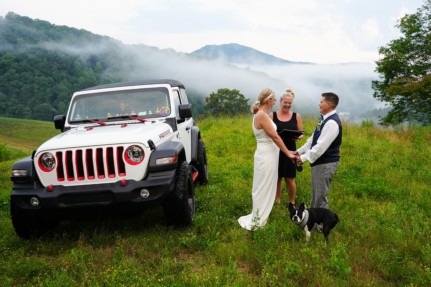 Two brides getting married by their white Jeep Wrangler at the mountain view at Honeysuckle Hills in Pigeon Forge with their boston terrier dog