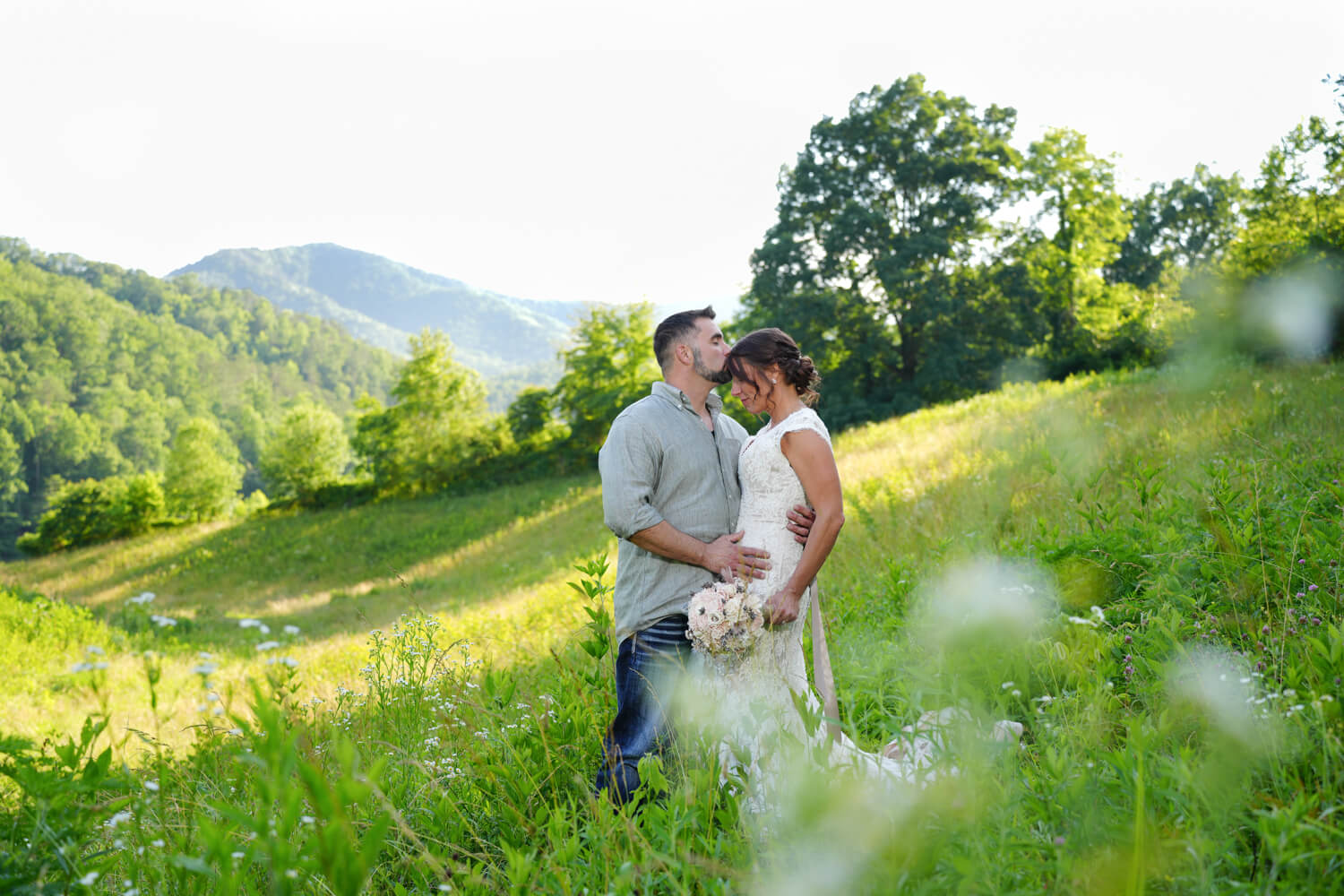 Casually dressed groom kissing his bride on the forehead in a meadow of white daisies at the mountain view at Honeysuckle Hills in Pigeon Forge
