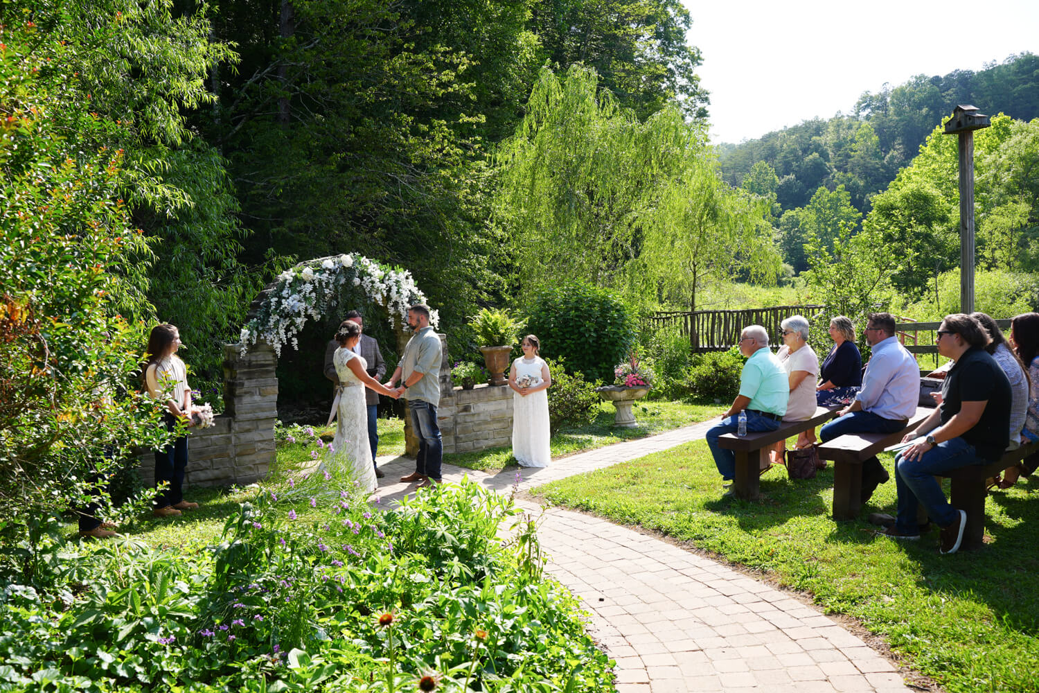 Path leading to a wedding ceremony at a stone arch with white flowers next to a garden at Honeysuckle Hills in Pigeon Forge