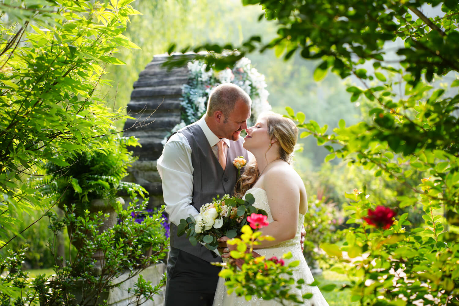 Wedding couple embracing in a kiss in a rose garden with a stone arch behind them at Honeysuckle Hills in Pigeon Forge TN