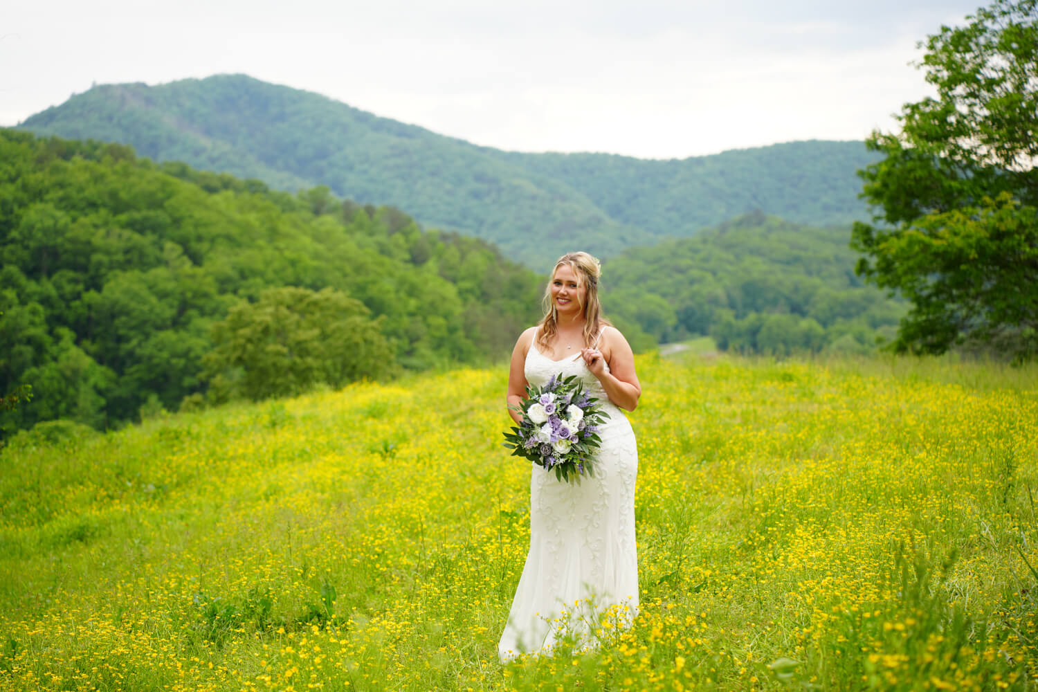 Bride playing with her hair and gazing with a smile on her face in a field of yellow buttercups at the mountain view at Honeysuckle Hills near the Great Smoky Mountains National Park in TN