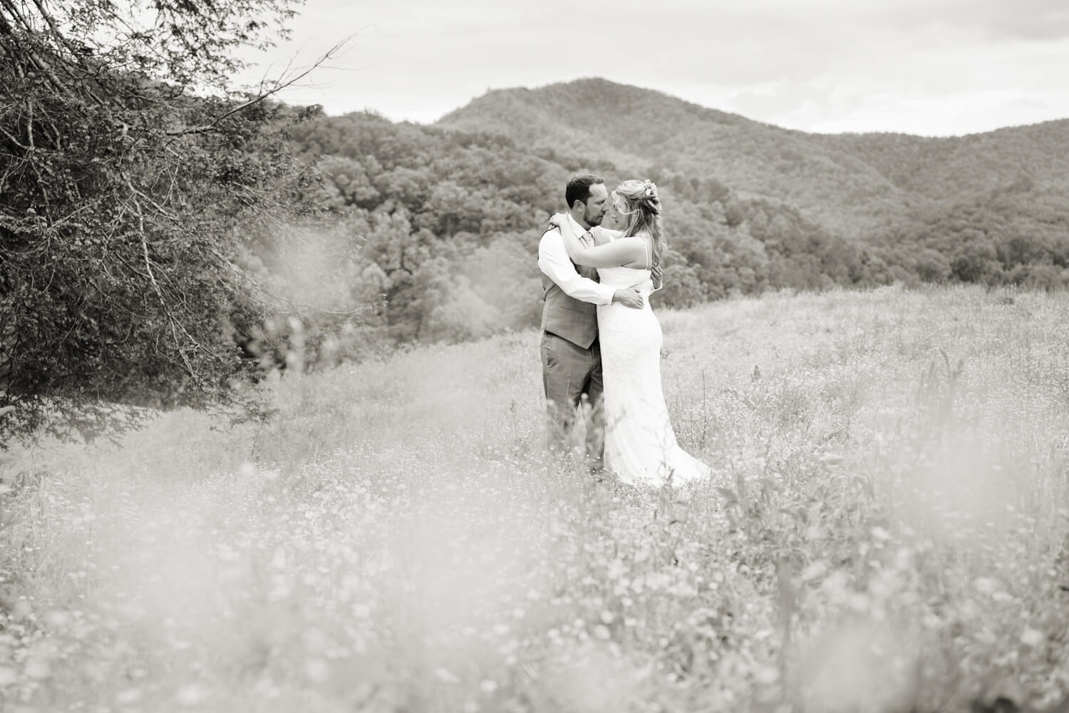 Black and White wedding photo of a couple kissing in a field with a soft floral foreground and mountain view background at Honeysuckle Hills near Gatlinburg TN