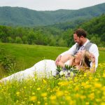 Bride laughing while laying in her groom's lap in a field of yellow buttercups at the mountain view adventure photography site at Honeysuckle Hills in Pigeon Forge TN