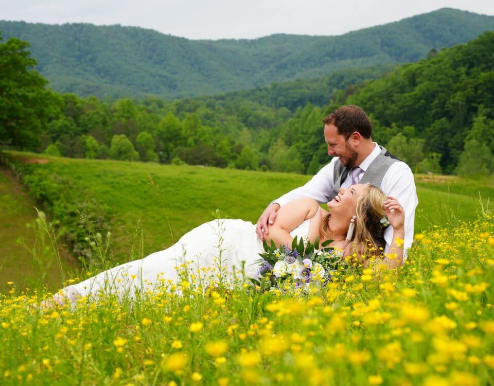 Bride laughing while laying in her groom's lap in a field of yellow buttercups at the mountain view adventure photography site at Honeysuckle Hills in Pigeon Forge TN