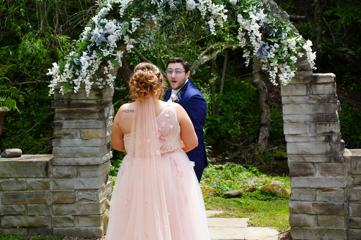 Groom in surprise seeing his bride for the first time by a stone archway