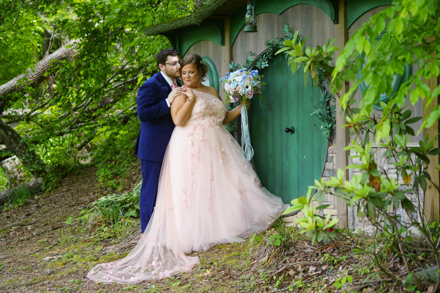 Wedding couple nestled closely together in a forest by a green fairy door that looks like a hobbit house at Honeysuckle Hills in Pigeon Forge