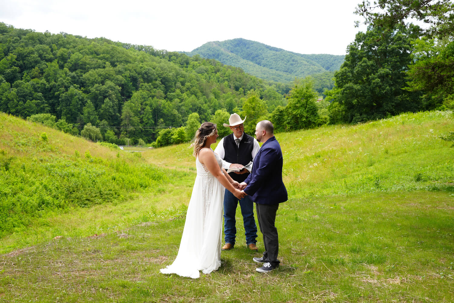 Western style minister in a cowboy hat marrying a couple in a field with a mountain behind them at Honeysuckle Hills near Gatlinburg TN