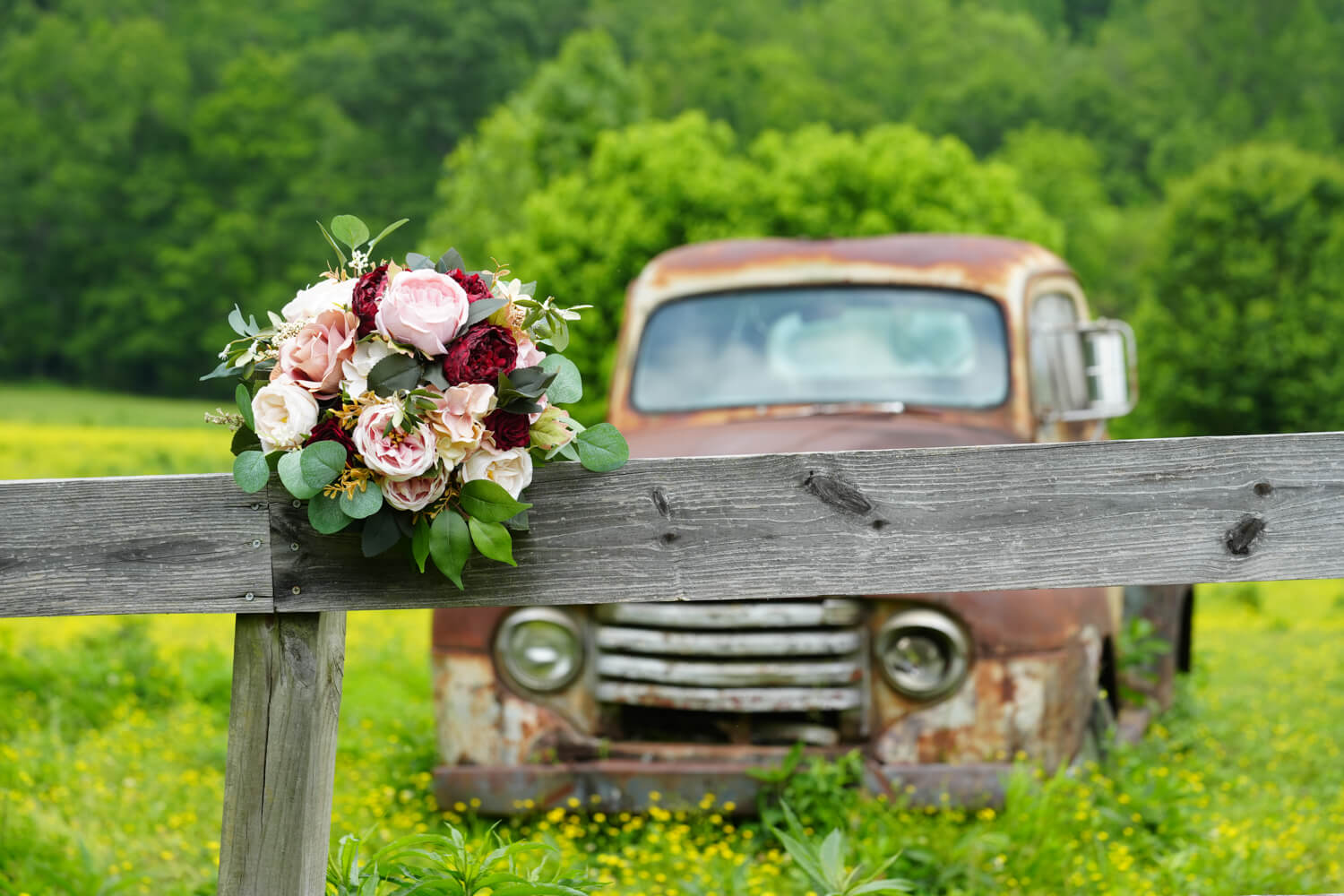 Bridal bouquet in pink and maroon sitting on a fence in front of an old Ford truck sitting in a field of yellow buttercups at Honeysuckle Hills in Pigeon Forge