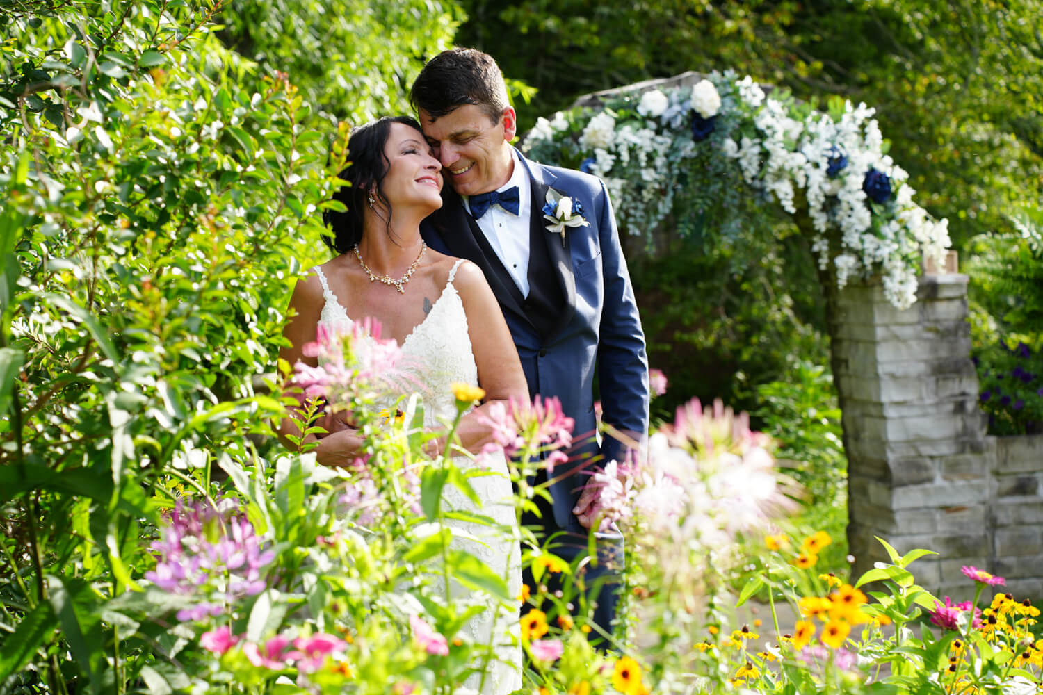 Wedding couple nuzzling each other in a wildflower garden by the stone arch at Honeysuckle Hills in Pigeon Forge