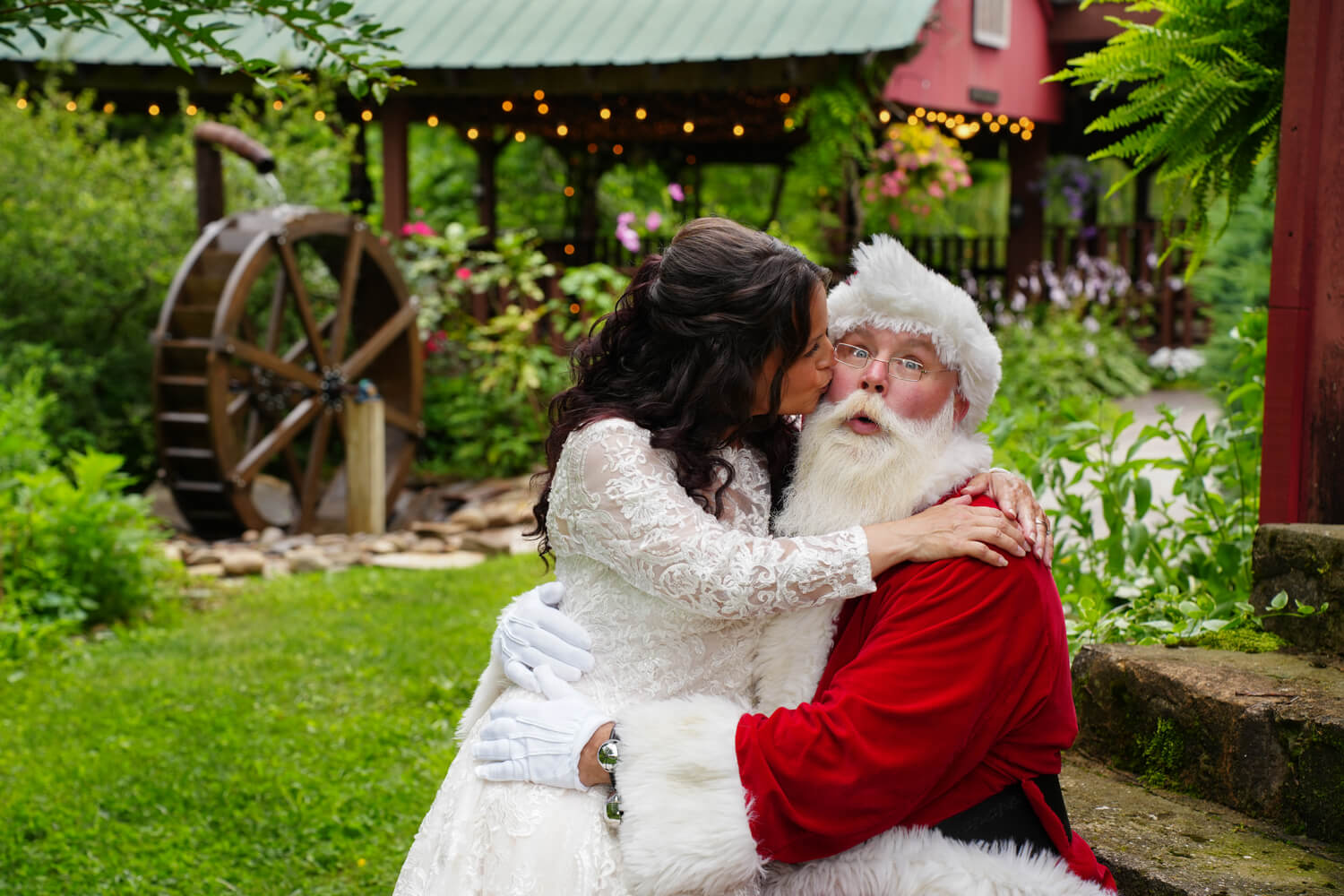 Santa and Mrs. Clause on their wedding day by a water wheel at Honeysuckle Hills in Pigeon Forge