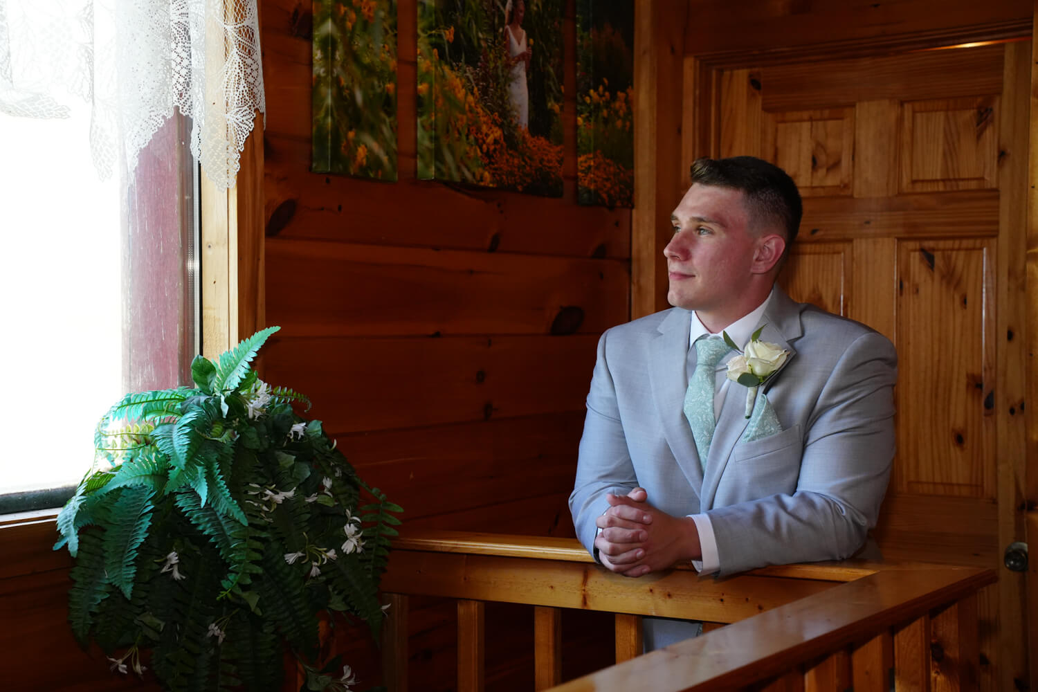 Groom looking out a window in a cabin style dressing room with pine walls