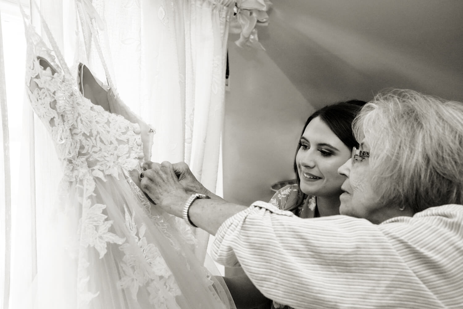 Grandmother helping her granddaughter with her wedding dress