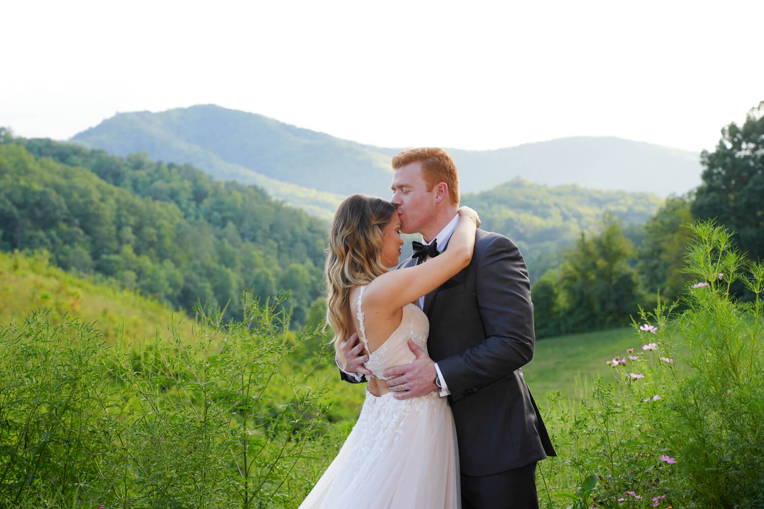 groom kissing his bride's forehead in a field with a mountain view in Pigeon Forge Tennessee
