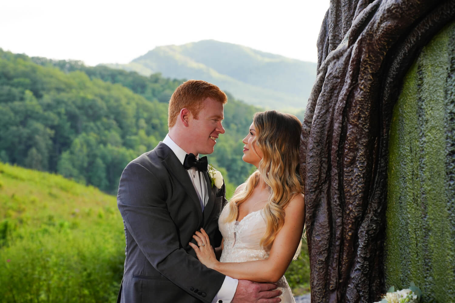 Wedding couple gazing into each other's eyes in front of a mountain view as the bride leans against a green door with log trim