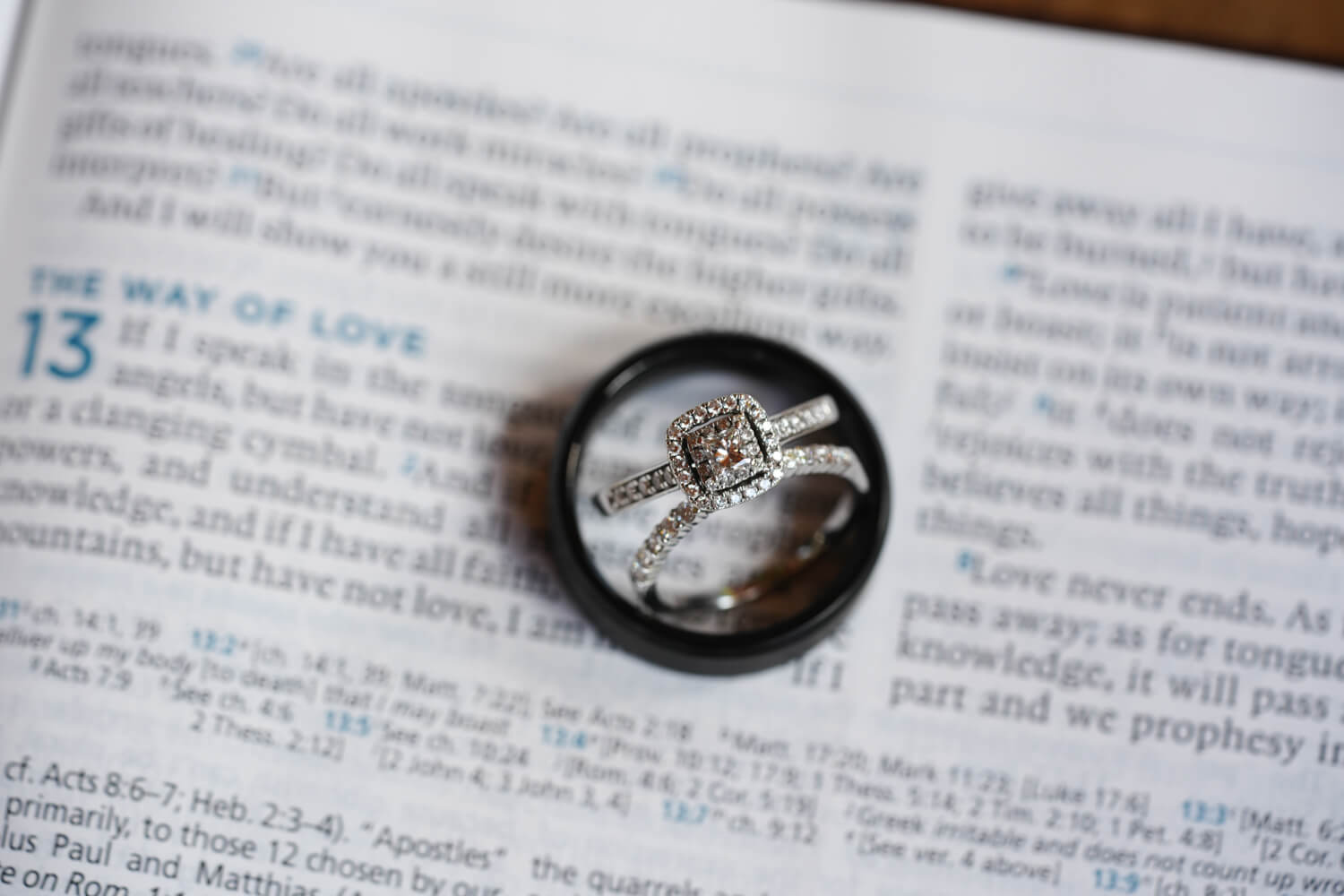 Black wedding band with silver wedding rings with diamonds inside it sitting on a Bible at a passage called the way of love