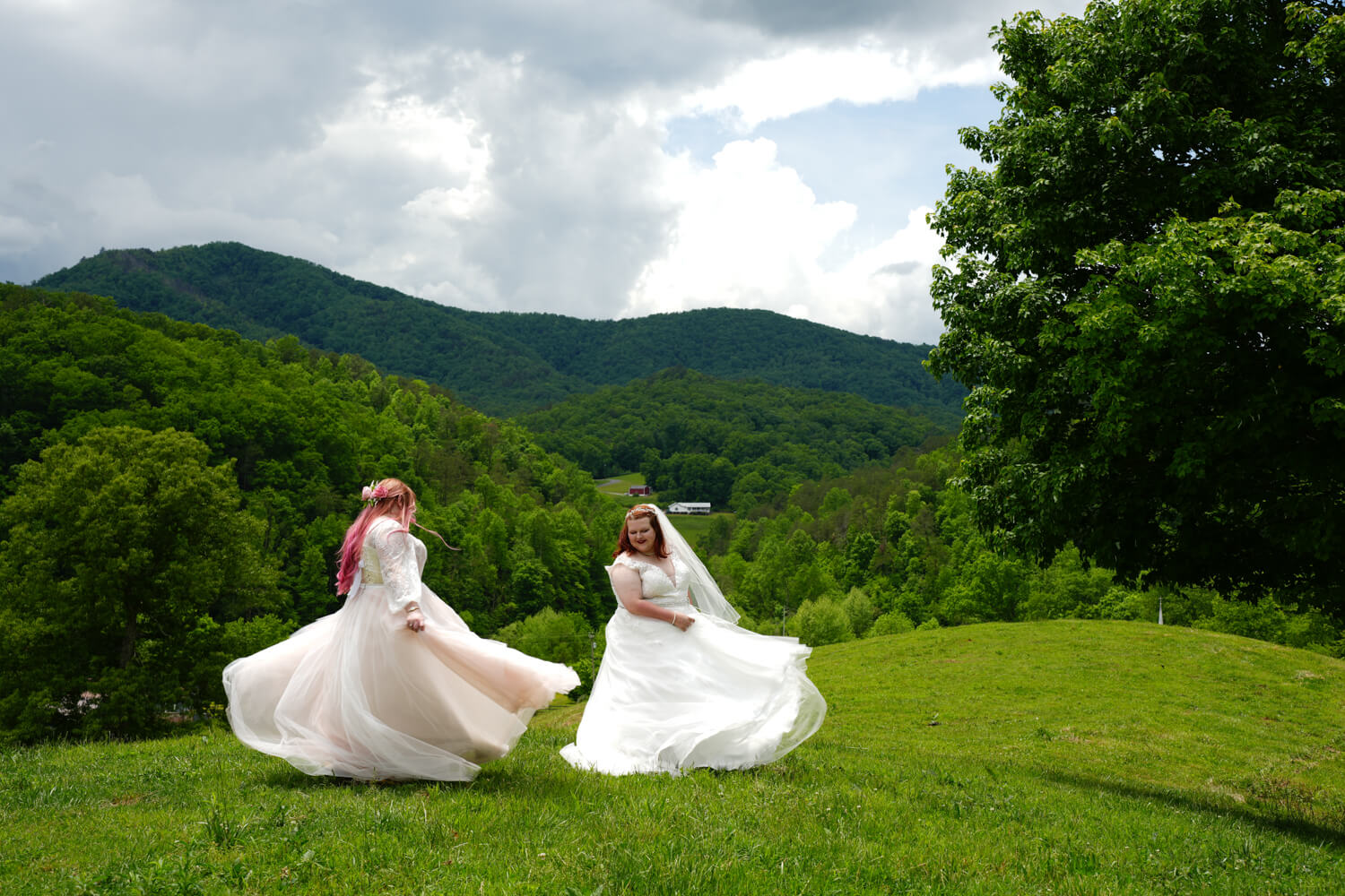 Two brides twirling around with flowing wedding dresses at a mountain view in the Smokies