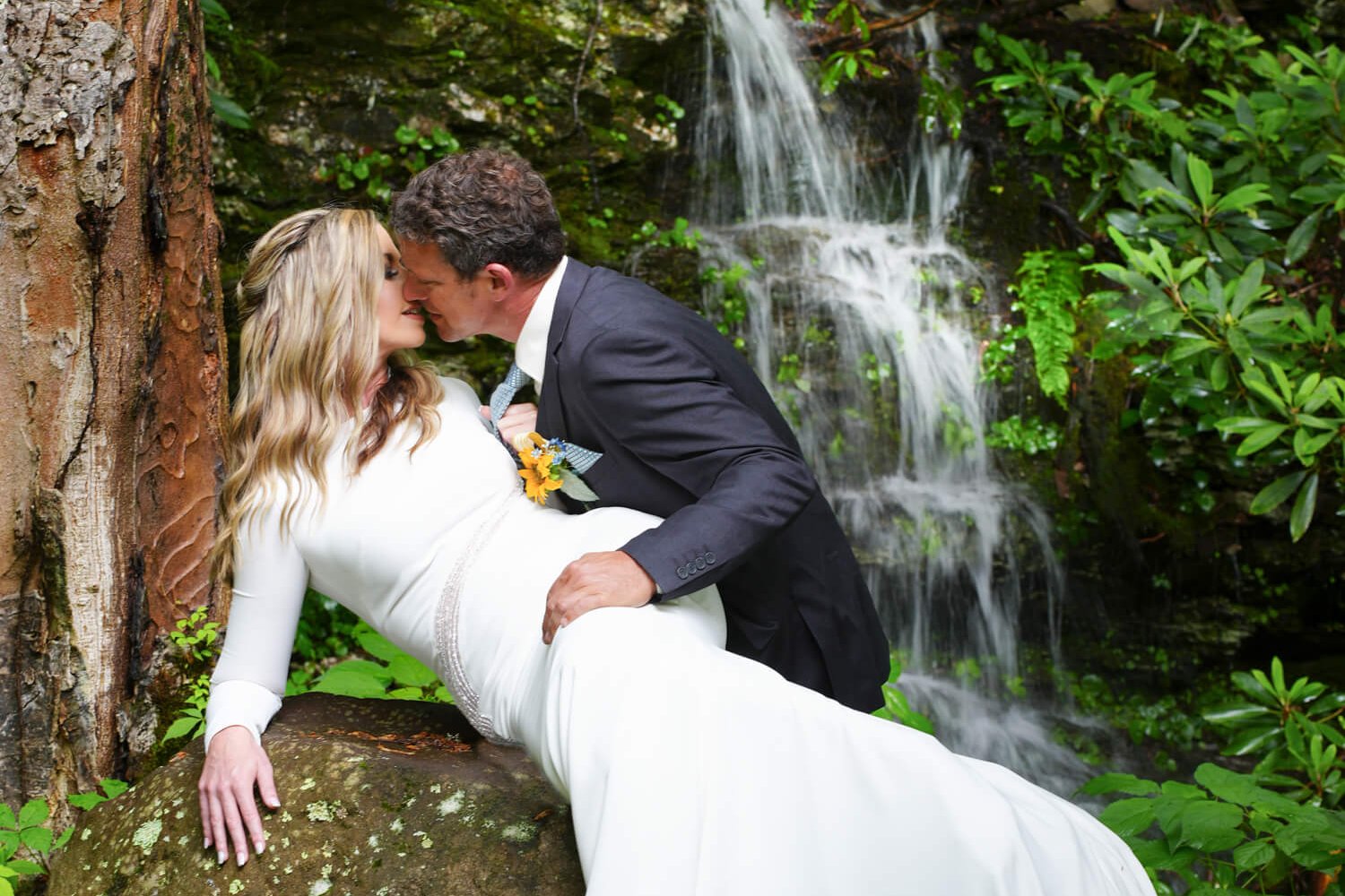 Groom kissing his bride passionately against a rock in front of a waterfall in the Smoky Mountains