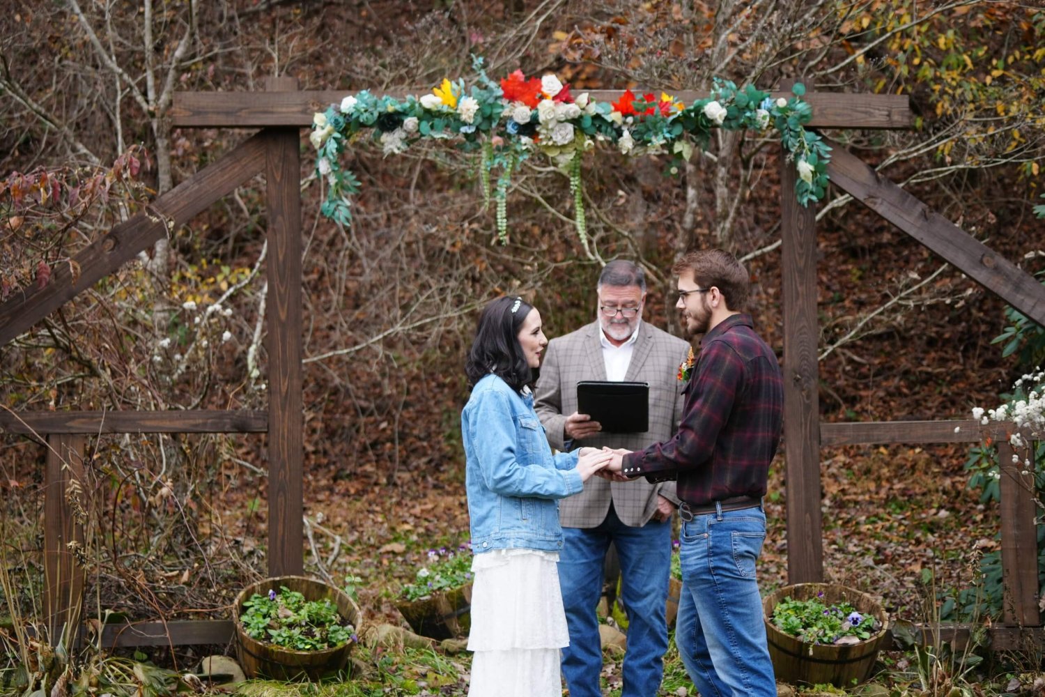 Simple wedding couple getting married in blue jeans and plaid at a wooden arbor with fall decor in the Smoky Mountains