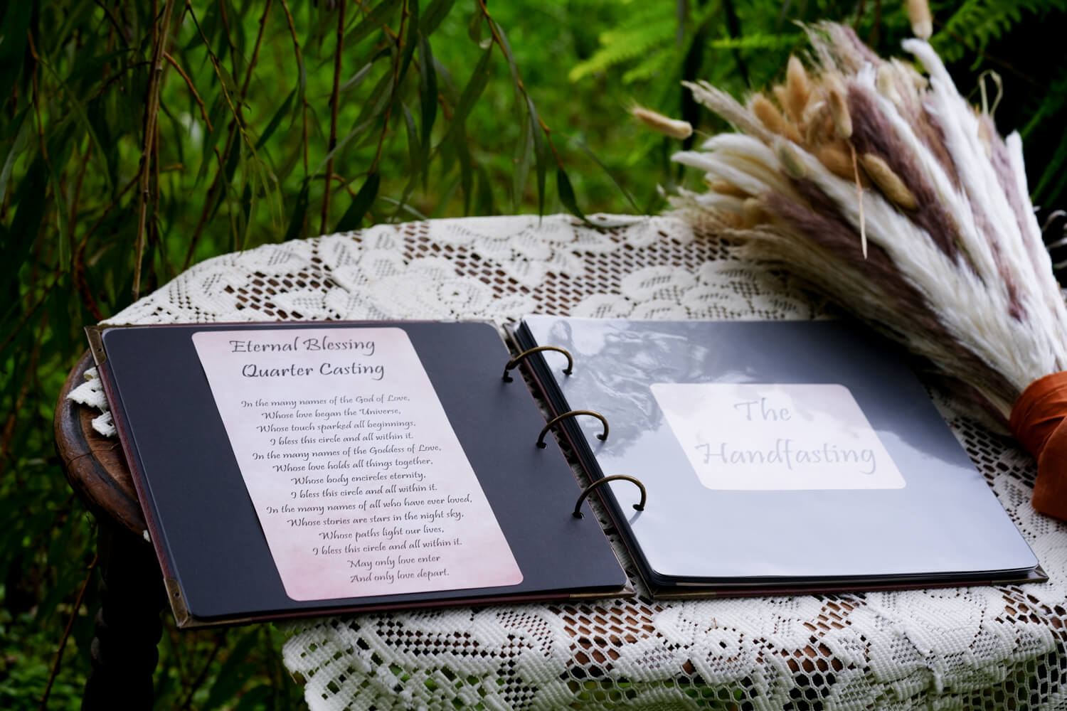 Book with hand fasting ceremony sitting on an antique table with lace cloth and a pampas grass wedding bouquet