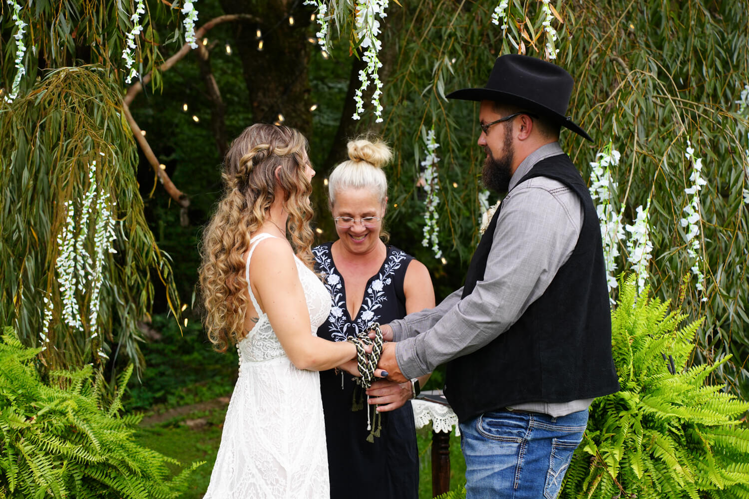 Officiant in black dress performing a hand fasting with green cords under a willow tree at Honeysuckle Hills in Pigeon Forge