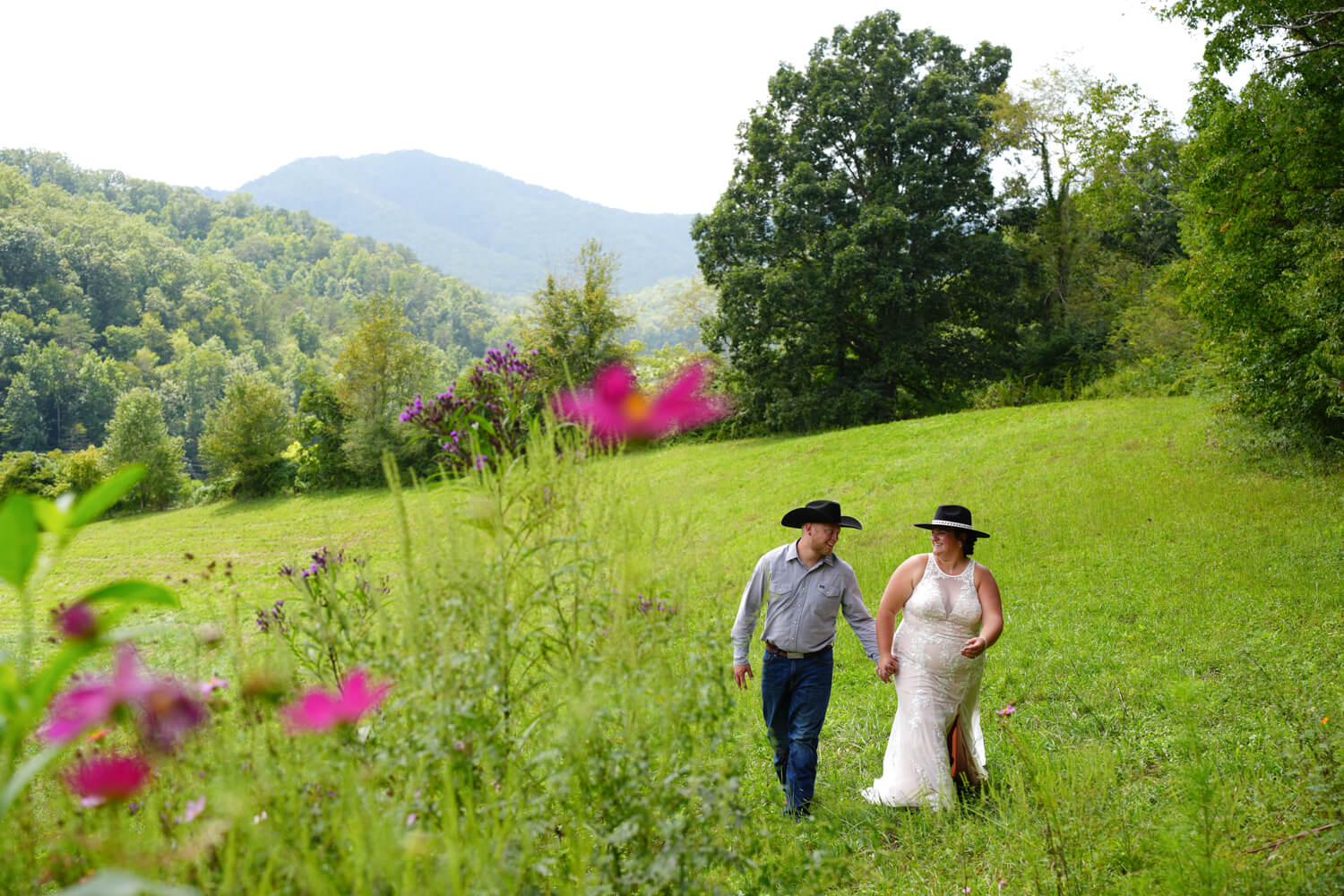 Western wedding couple with black cowboy hats walking in a meadow with a mountain ridge background in Gatlinburg Tennessee