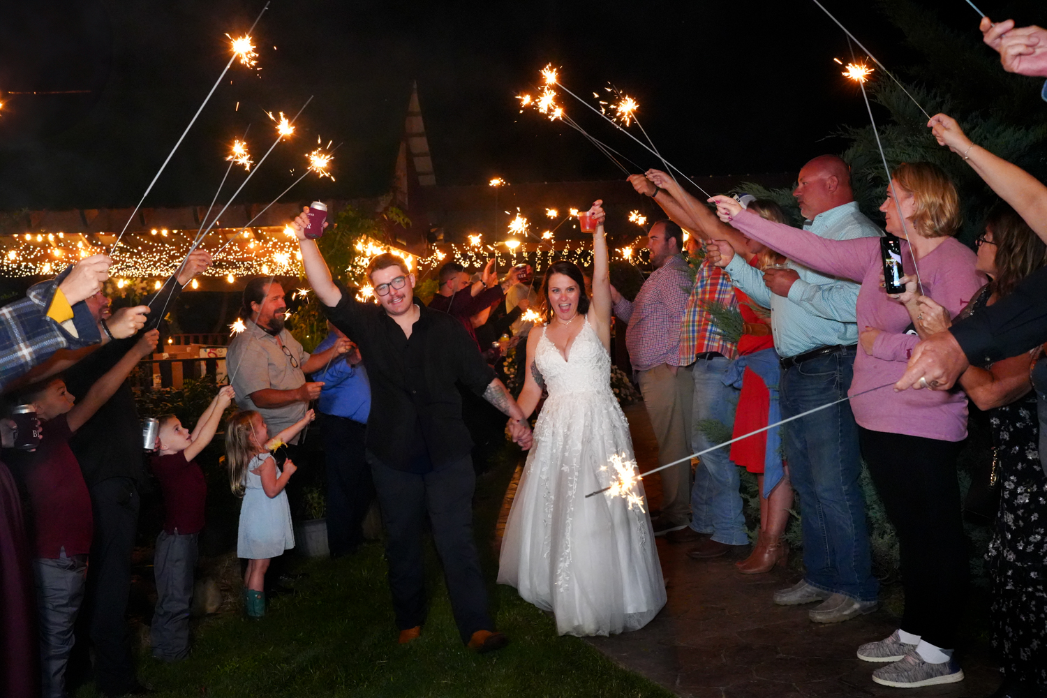 Bride and Groom with arm raised high in celebration during a sparkler exit at their wedding reception