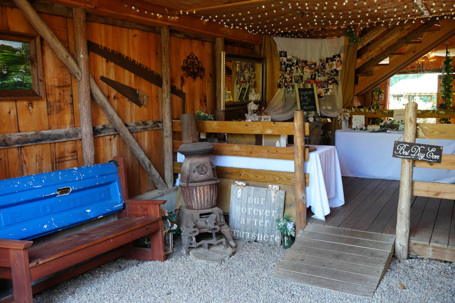 Entry to a country chic barn wedding venue with Blue Ford tailgate bench, old stove and tables with white cloths for wedding decor