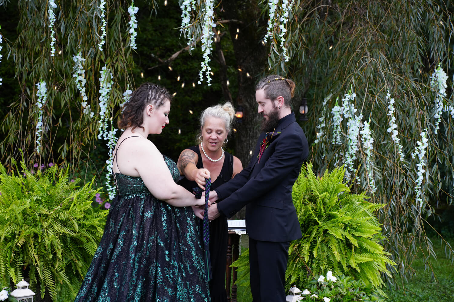 Hand fasting ceremony with dark green cords under a willow tree with white wisteria at Honeysuckle Hills in Pigeon Forge Tennessee