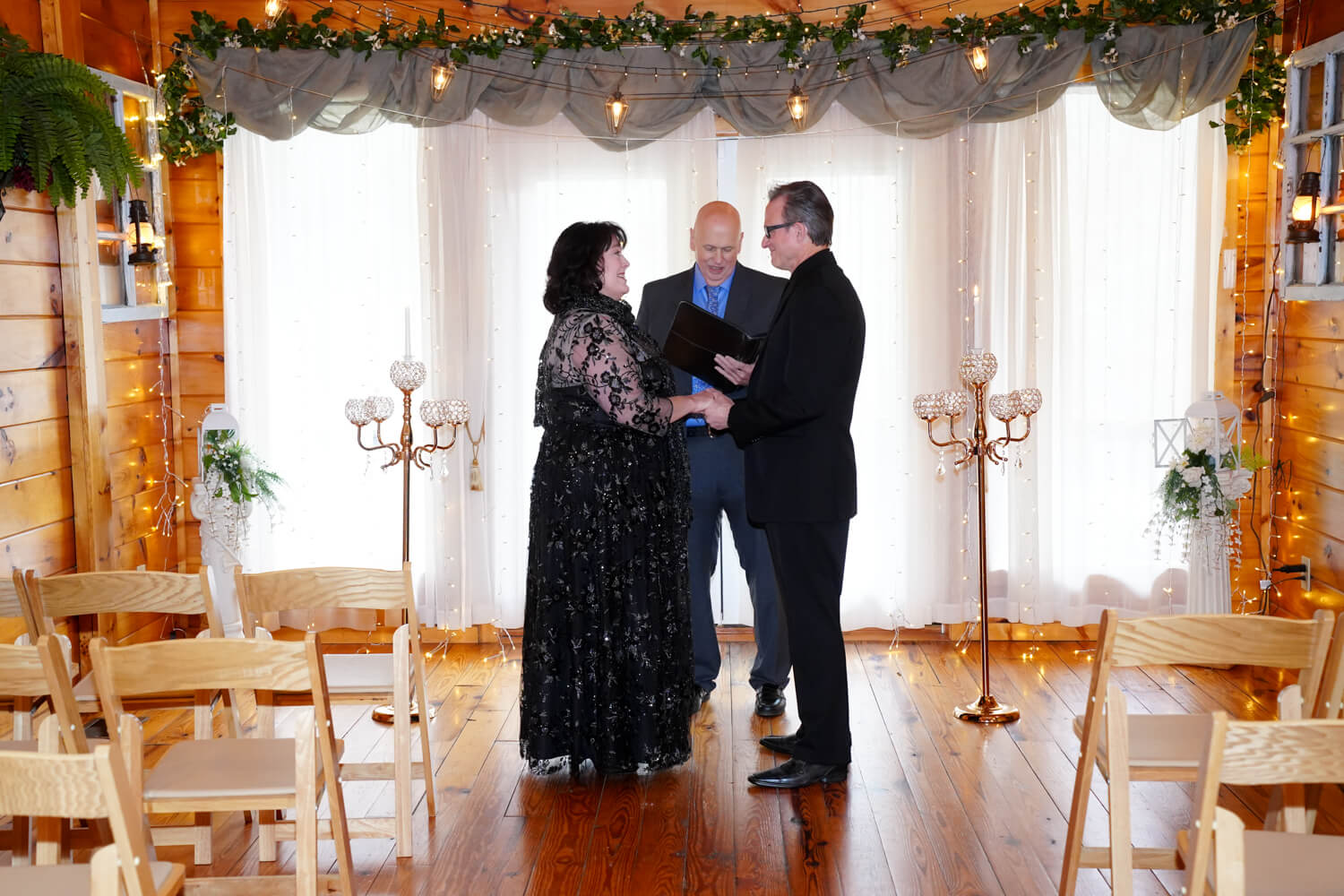 Couple getting married in black wedding attire in a wedding chapel with string lights and candles